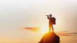 person with telescope standing on a rock